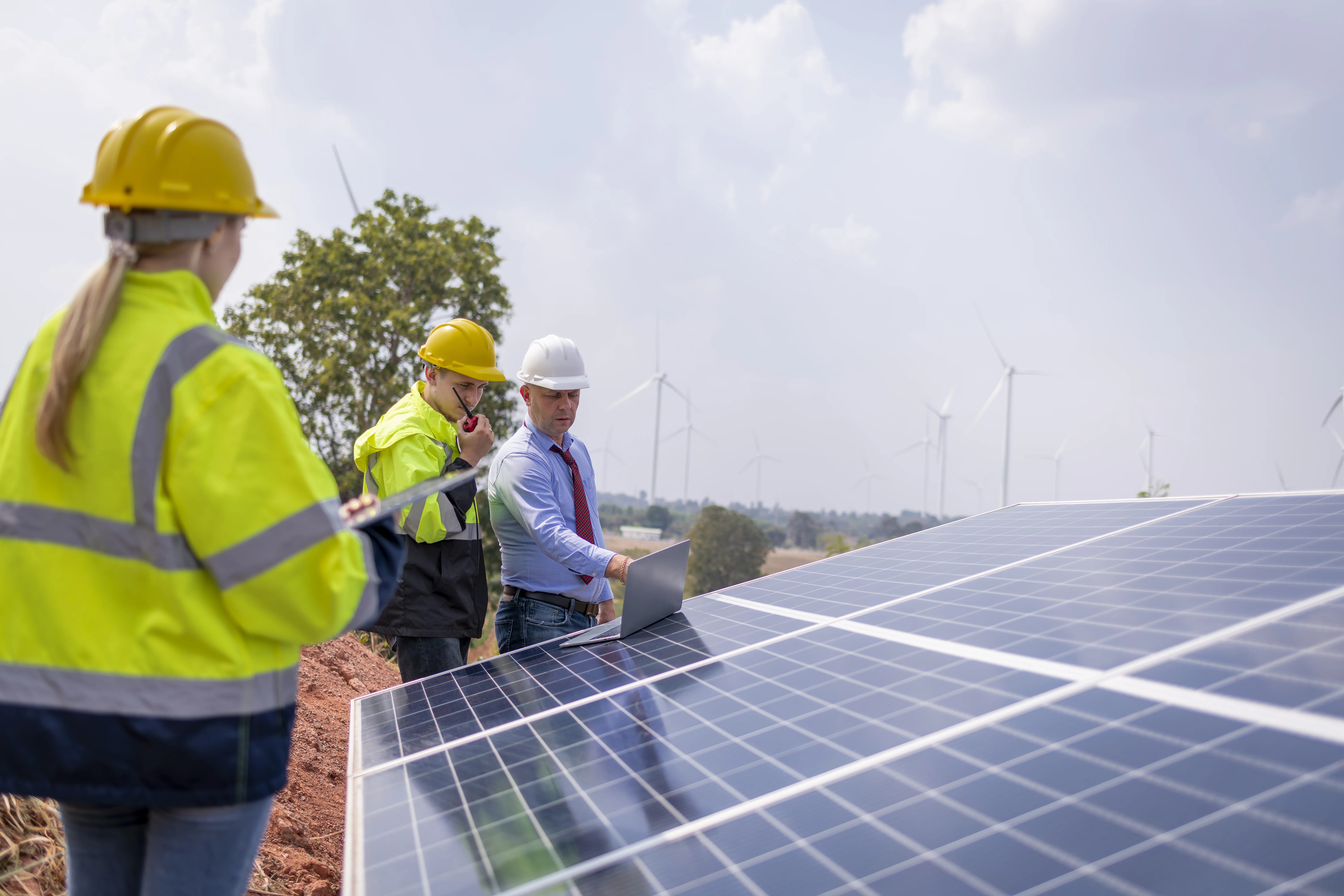 Workers installing solar panels with wind turbines in background